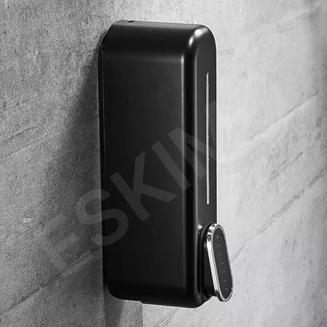 A close-up, angled view of a black wall-mounted soap dispenser against a textured gray wall.