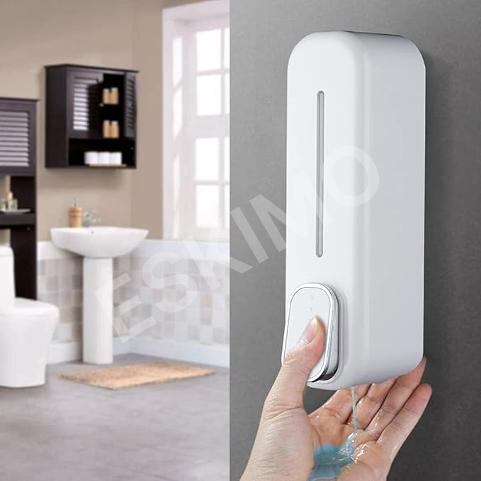 A white wall-mounted soap dispenser in a bathroom, with a hand pressing the button to dispense soap into a palm.